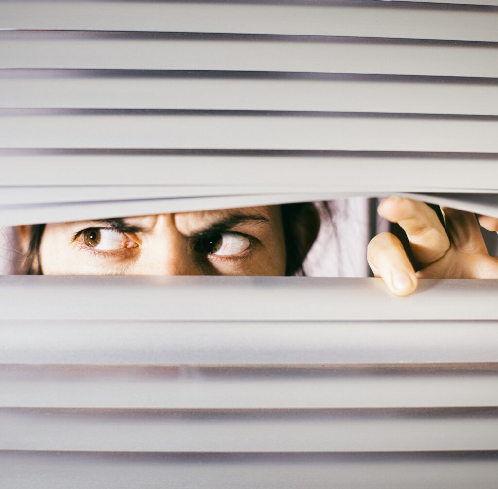 Young woman peering anxiously through blinds