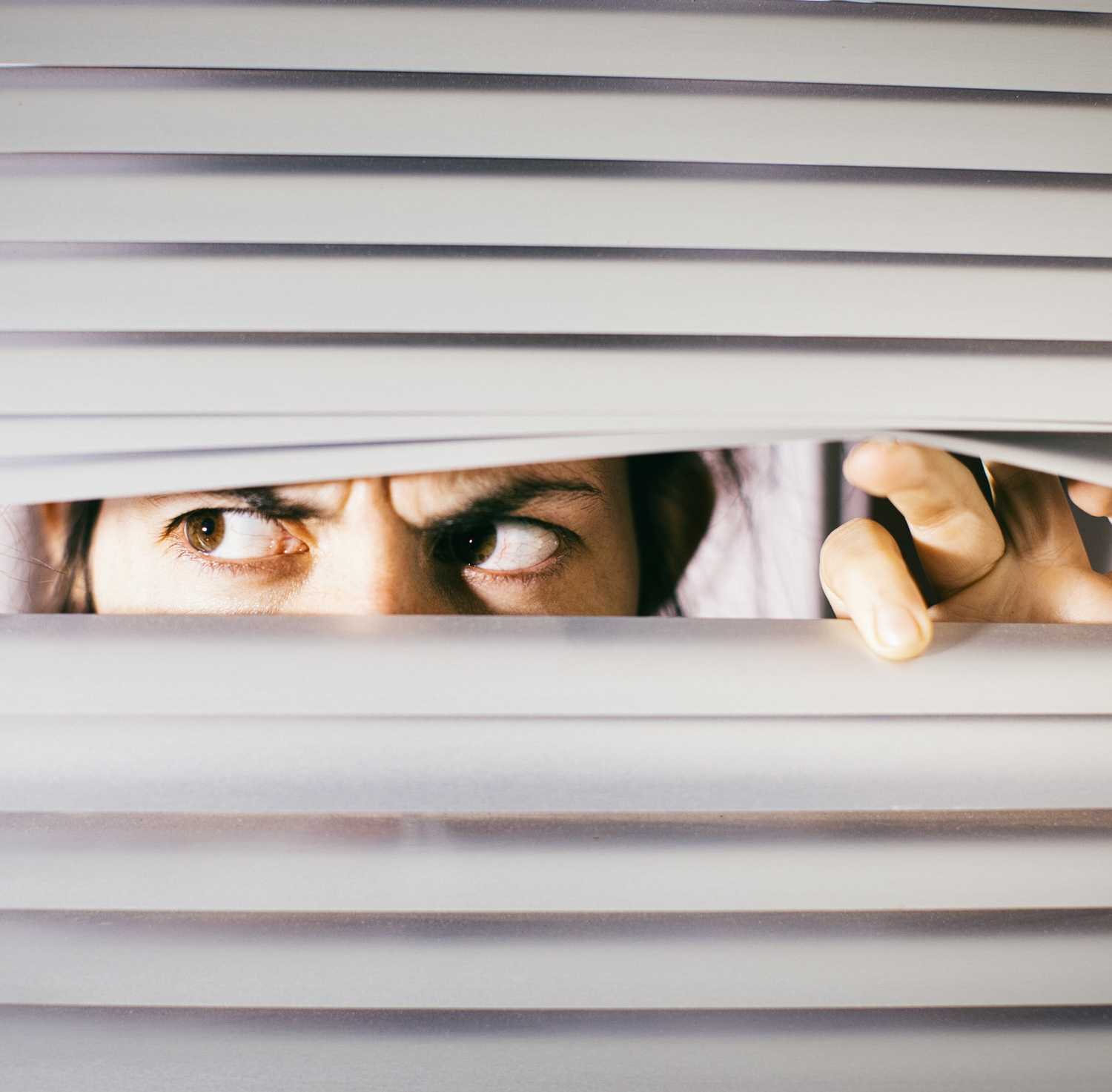 Young woman peering anxiously through blinds